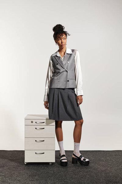 A young woman in chic business attire poses gracefully by a filing cabinet.