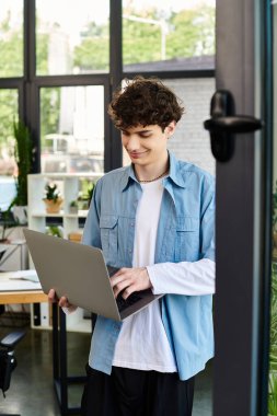 Bir adam, çağdaş bir ofis ortamında dururken dizüstü bilgisayarda yazmaya odaklanır..