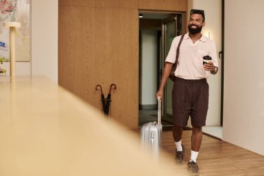 Neşeli bir adam zarif bir otel lobisinde geziyor, rahatlatıcı bir tatile hazır..