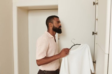 İyi giyimli bir Afro-Amerikan erkeği seyahat ederken çağdaş bir otel odasında kıyafet seçer..