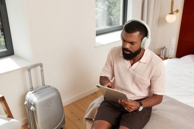 Modern bir otel odasında şık bir adam seyahat seçeneklerini gözden geçirmek için tablet kullanır..