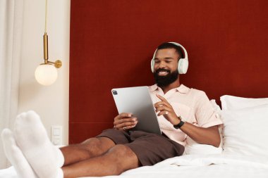 Modern bir otel odasında tablet kullanırken eğlenen şık bir adam..