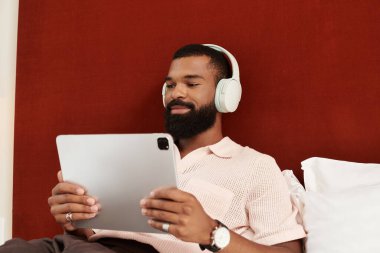 Yakışıklı bir Afrikalı Amerikalı adam, tabletinin tadını çıkarırken şık bir otel odasında dinleniyor..