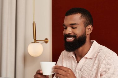 Yakışıklı bir Afrikalı Amerikalı, modern bir otel odasında dinlenirken kahvesini yudumluyor..
