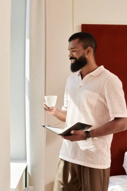 Afro-Amerikan bir adam çağdaş bir otel odasında bir fincan kahve içiyor..