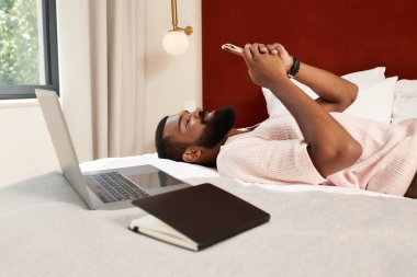 Yakışıklı bir adam şık bir otel odasında, telefonuna bakmaktan zevk alır..