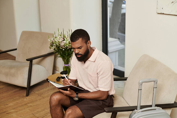 A handsome African American man writes in a notebook while relaxing in a chic hotel lobby.