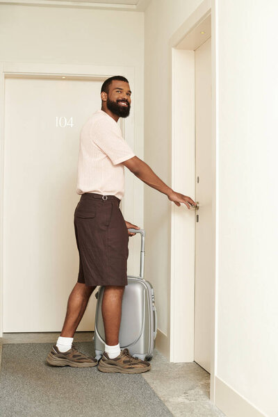 Счастливый путешественник стоит у лифта со своим чемоданом, готовый к новым приключениям.