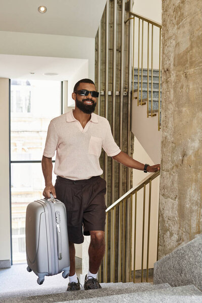 A stylish and charming African American man walks confidently in a hotel, ready for adventure.