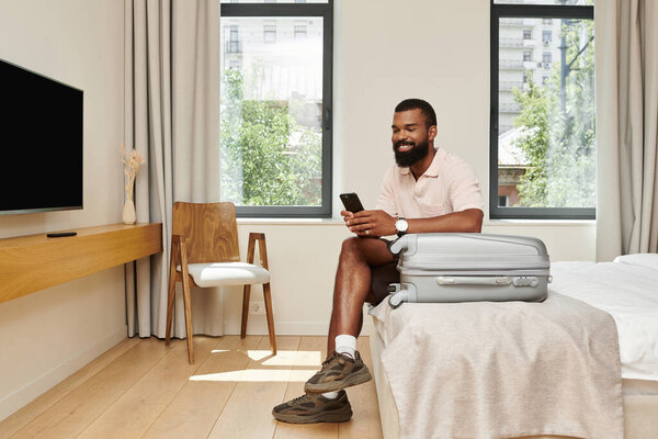 Симпатичный афроамериканец расслабляется в шикарном номере отеля, проверяя телефон..