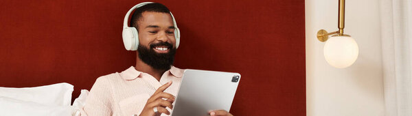 A stylish African American man smiles while using a tablet in his hotel room during vacation, banner