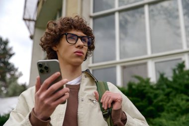 Kıvırcık saçlı genç bir adam garip bir şekilde akıllı telefonunu kontrol ediyor..