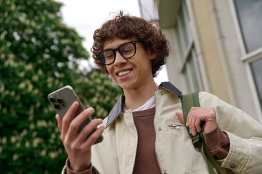 Genç ve yakışıklı bir öğrenci, telefonunu kontrol ederken gülümsüyor..