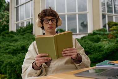 Öğrenci dışarıda kitapla, kulaklıklarla, sakin bir ortamda rahatlıyor..