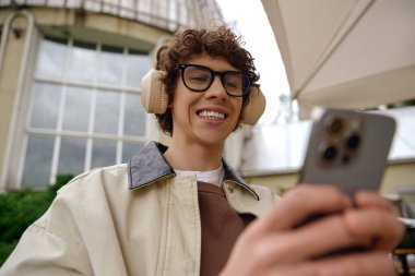 Genç ve yakışıklı bir öğrenci dışarıda neşeli bir yürüyüş yapıyor, akıllı telefonuna dalmış..