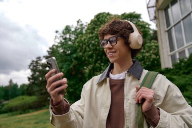 Genç bir adam dışarıda geziniyor, akıllı telefonuyla arkadaşlarıyla iletişim kurarken gülümsüyor..