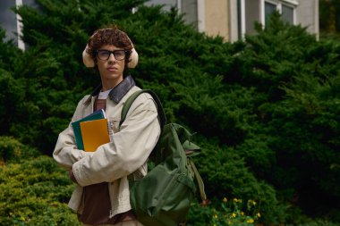 Şık gözlükler ve kulaklıklar takmış genç bir adam elinde defterlerle dışarıda geziniyor..