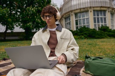 Yakışıklı genç adam çimlerde dizüstü bilgisayarla oturuyor, sakin açık hava ortamında çalışmalara odaklanmış..