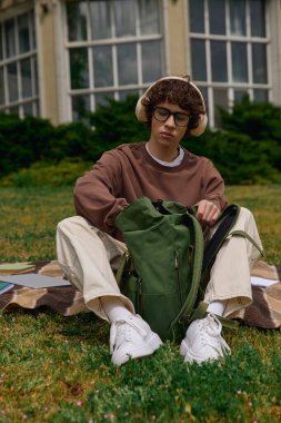 Kıvırcık saçlı genç bir adam kampüste geziyor, güneşin ve yeşilliğin tadını çıkarıyor..