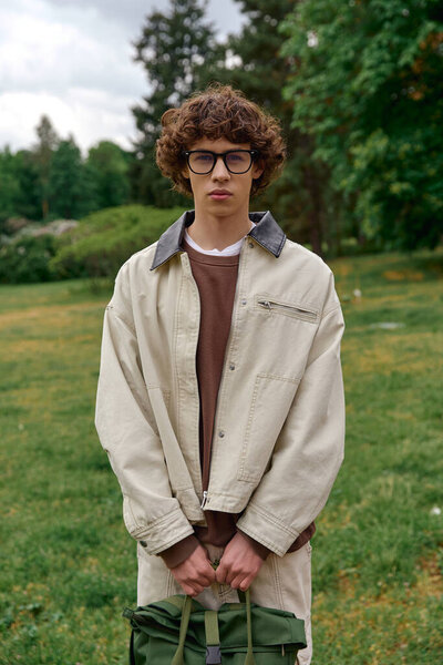 Красивый молодой студент прогуливается по пышной зеленой зоне, размышляя о своем путешествии и целях.