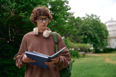 Genç ve yakışıklı bir öğrenci, doğanın ortasında kitap okuyarak, dışarıda huzurlu bir yürüyüş yapıyor..