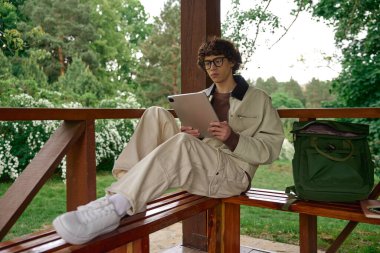 Yakışıklı genç bir adam yemyeşil bir parkta tabletine dalmış bir bankta dinleniyor..