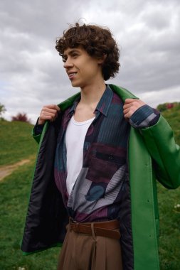 Yakışıklı genç adam yeşil doğayla çevrili bir yolda yürüyor ve modaya uygun kıyafetler giyiyor..