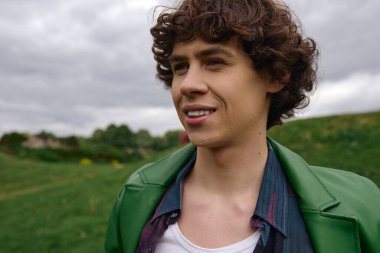 Kendine güvenen genç bir adam, canlı giyinmiş, yemyeşil bir alanda rahat bir yürüyüş yapar..