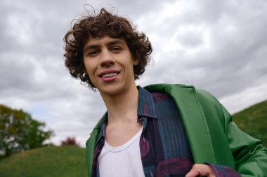 Karizmatik bir öğrenci bulutlu bir gökyüzünün altında gülerek verimli bir arazide gezinir..