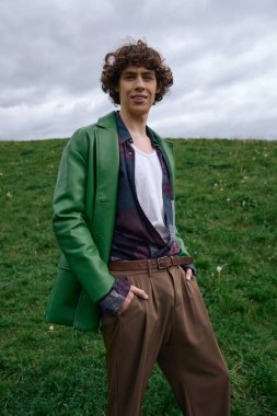 Genç bir adam açık havada gezer, yemyeşil manzaranın ortasında şık bir kıyafet sergiler..