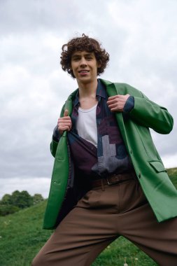 Kıvırcık saçlı yakışıklı öğrenci dışarıda dolaşıyor, doğayı kucaklıyor ve modasını sergiliyor..