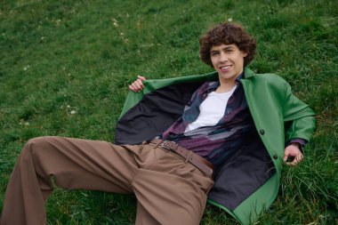 Genç ve yakışıklı bir öğrenci çimenlerin üzerinde rahatlar. Etrafı güzelliklerle çevriliyken gülümser..