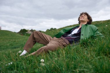 Neşeli genç bir adam çimenli bir yamaçta dinleniyor, doğanın dinginliğini kucaklıyor..