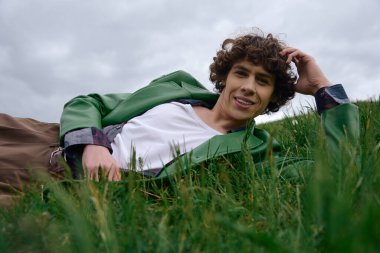 Yeşil ceketli genç adam açık havada sakin bir deneyimin tadını çıkarırken taze çimenlerde dinleniyor..