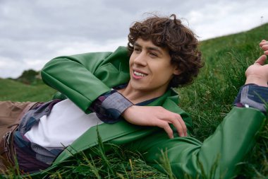 Genç, yakışıklı bir öğrenci çimenlerde rahatlar, gülümser ve açık havada sırılsıklam olur..