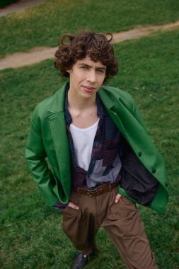 Yakışıklı genç bir adam yeşil bir parkta şık bir ceket ve rahat bir kıyafet giyerek dolaşır..