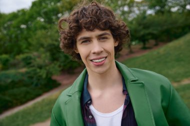 Parlak ve neşeli genç adam manzaralı bir parkta geziniyor, neşe ve güven saçıyor..