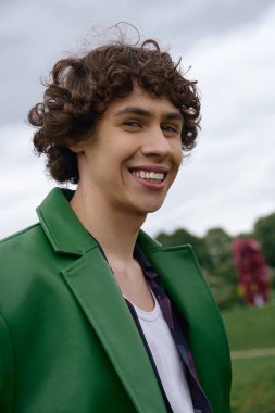 Yakışıklı genç bir adam açık hava parkında dolaşır, zarif yeşil bir ceketle doğayı kucaklar..