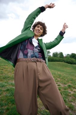 Neşeli bir öğrenci yeşil bir arazide yürüyor, şık kıyafetleriyle neşe ve özgürlüğü kucaklıyor..