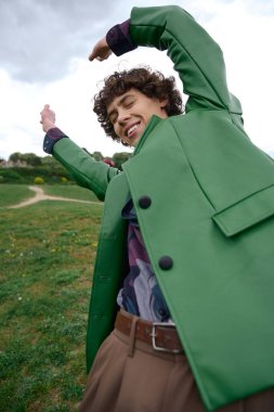 Neşeli genç bir adam canlı yeşil bir paltoyla dışarıda geziniyor, doğal güzelliğin tadını çıkarıyor..
