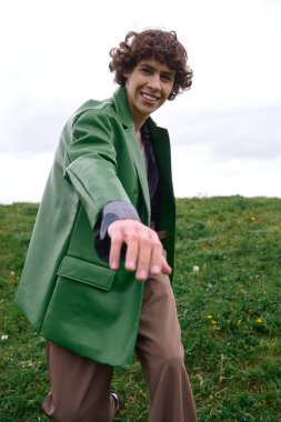 Neşeli genç bir adam kendine güvenen yeşil bir ceketle dolaşırken doğada mutlu bir şekilde gülümsüyor..