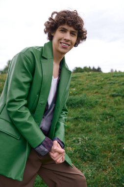 Yeşil ceketli genç bir adam çimenli bir açık havada mutlu mesut dolaşır..