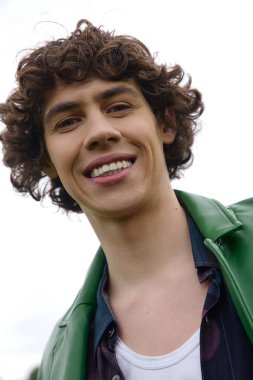 Kıvırcık saçlı genç bir adam açık alanda geziniyor, açık havanın güzelliğini kucaklıyor..