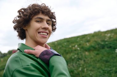 Neşeli genç bir adam, canlı yeşillikler ve yumuşak bulutlarla çevrili açık havada yürüyor..