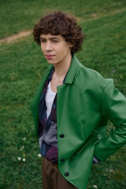 Yakışıklı genç bir adam yemyeşil bir arazide özgüven yayarak düşünceli bir yürüyüş yapar..