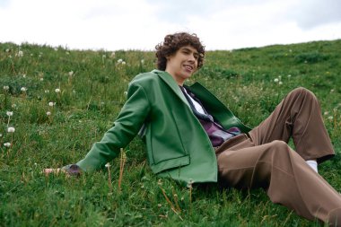 Parlak öğleden sonra ışığı yumuşak çimenlerde oturan genç bir adamı vurguluyor. Huzurun tadını çıkarıyor..