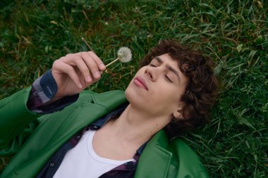 Genç bir adam çimenlerde yatıyor, düşüncelere dalmış, elinde nazikçe bir karahindiba esintisi tutuyor..