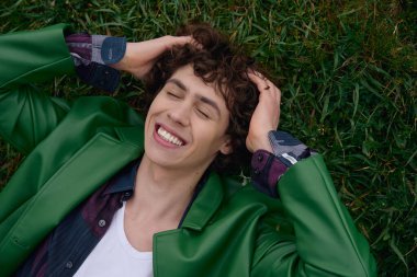 Neşeli, genç bir erkek öğrenci açık havada gülümseyen ve rahatlamış bir şekilde yürüyor..