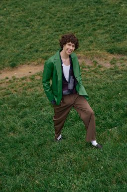 Genç bir adam, güneşli bir günde yeşil çimlerde dolaşırken çevresini inceliyor..