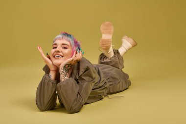 Kısa, renkli saçlı neşeli genç bir kadın, yumuşak bir arka planla neşeli bir şekilde stüdyoda poz veriyor..